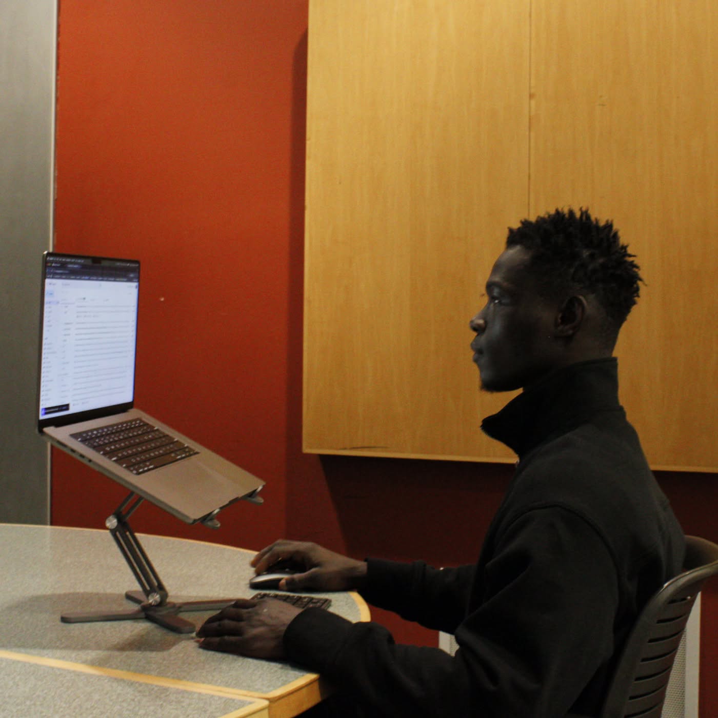 background: #8f8f8f;
background: linear-gradient(90deg, rgba(143, 143, 143, 1) 0%, rgba(31, 31, 31, 1) 71%);
Person using a laptop on a stand in an office setting with a red wall.